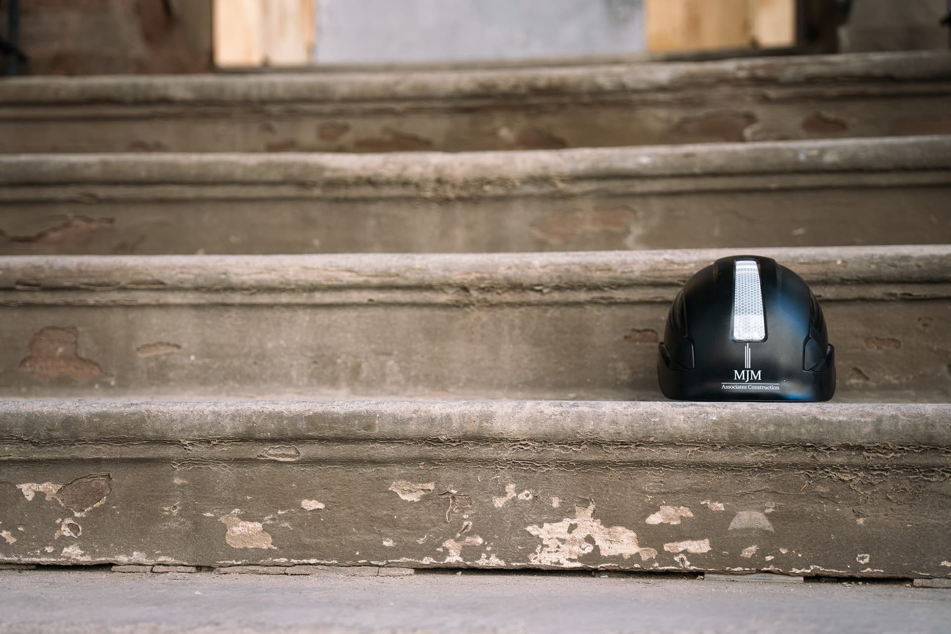 MJM Associates branded hard hat resting on construction site steps